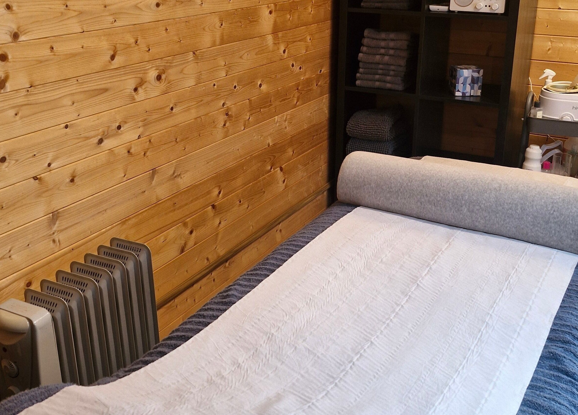 Massage room at Bare Essential Beauty, Addington, England, featuring a wooden interior and cozy massage bed.