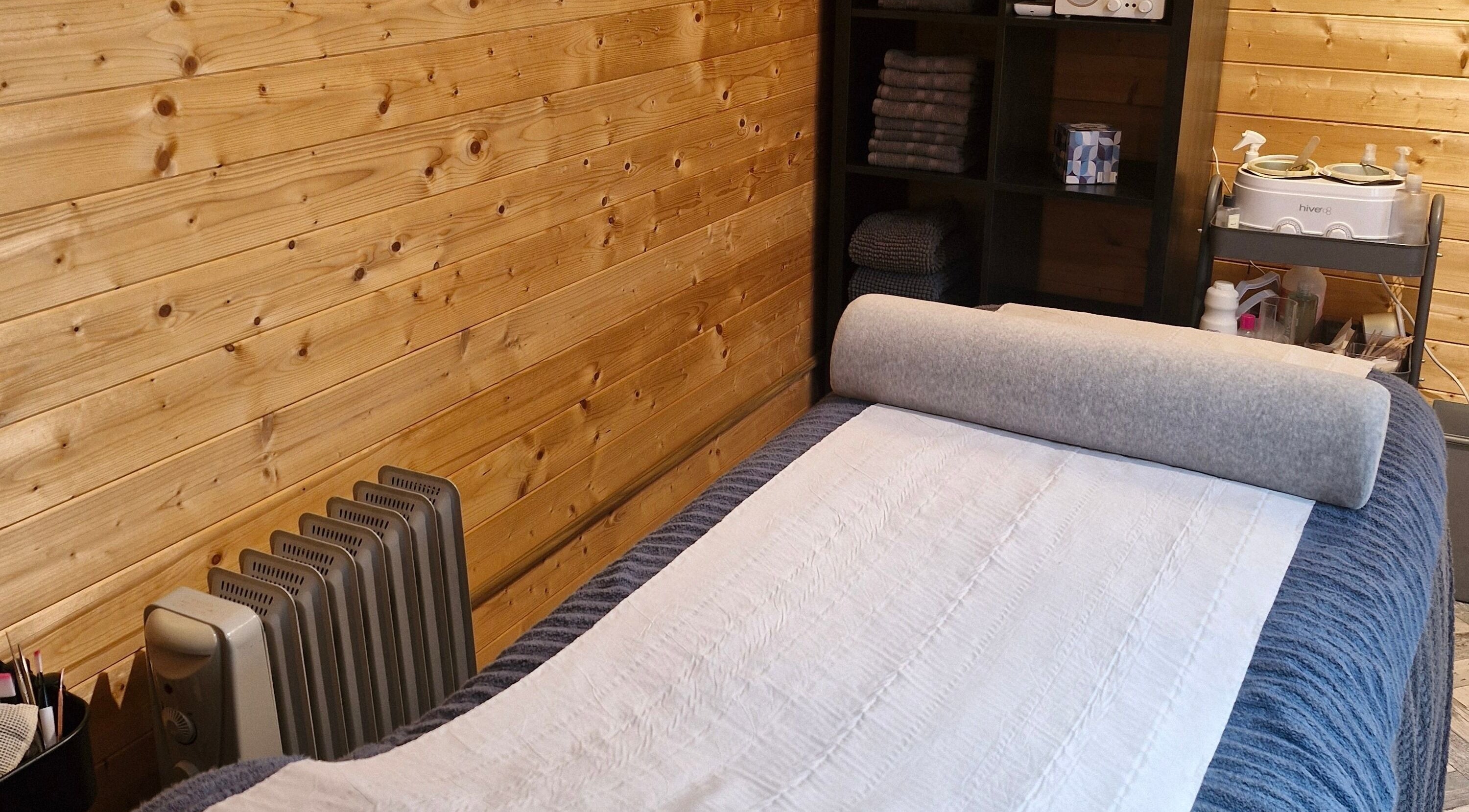 Massage room at Bare Essential Beauty, Addington, England, featuring a wooden interior and cozy massage bed.
