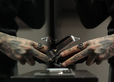 Tattooed hands holding a clipper at Cutz Hair Studio, Riyadh, SA, showcasing skilled barber work.