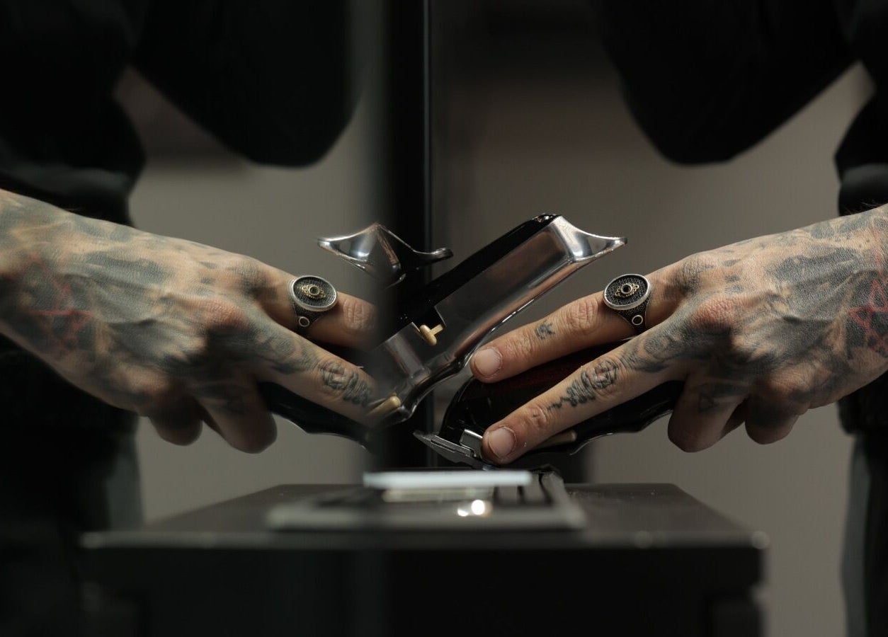Tattooed hands adjusting clippers at Cutz Hair Studio Premium, Riyadh, Riyadh Province, SA.