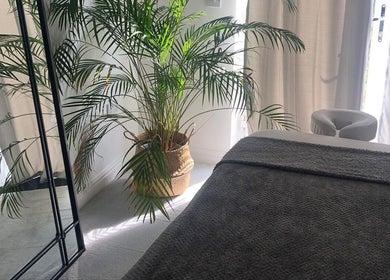 Serene massage room at Waseley Wellbeing, Worcestershire, GB, featuring a cozy bed and lush plant decor.