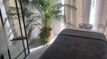 Serene massage room at Waseley Wellbeing, Worcestershire, GB, featuring a cozy bed and lush plant decor.