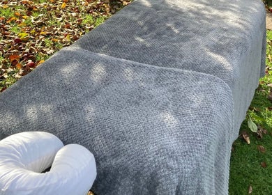 Outdoor massage table with soft gray blanket at Waseley Wellbeing, Worcestershire, GB surrounded by autumn leaves.