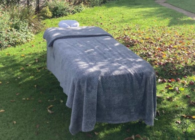 Outdoor massage table at Waseley Wellbeing, Worcestershire, GB, surrounded by lush greenery.