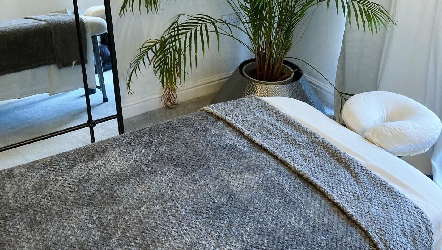 Relaxing massage room at Waseley Wellbeing, Worcestershire, GB, featuring a cozy treatment table and lush plant.