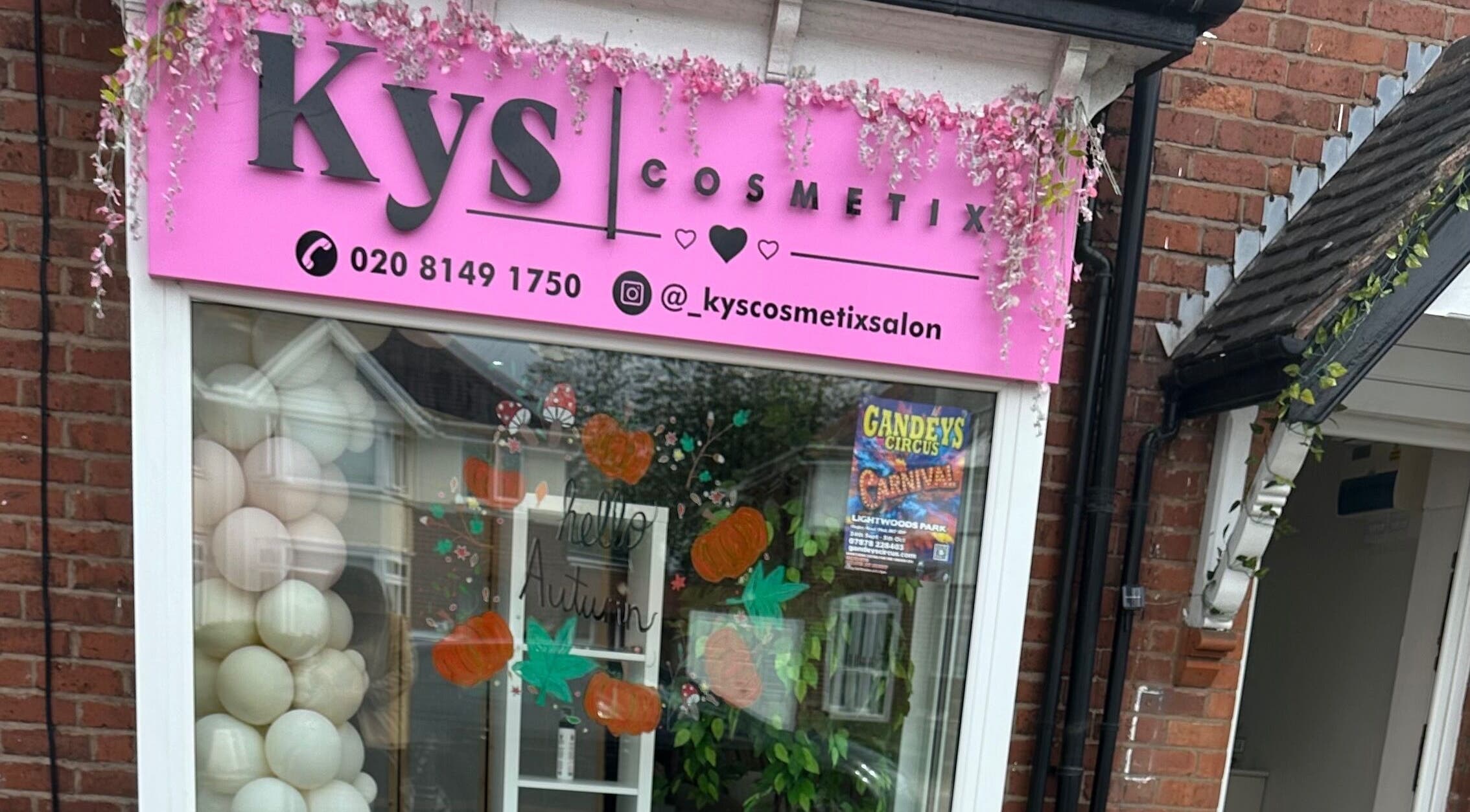 Exterior of Kyscosmetix Salon in Birmingham, England, GB, featuring a pink sign and decorative autumn window display.