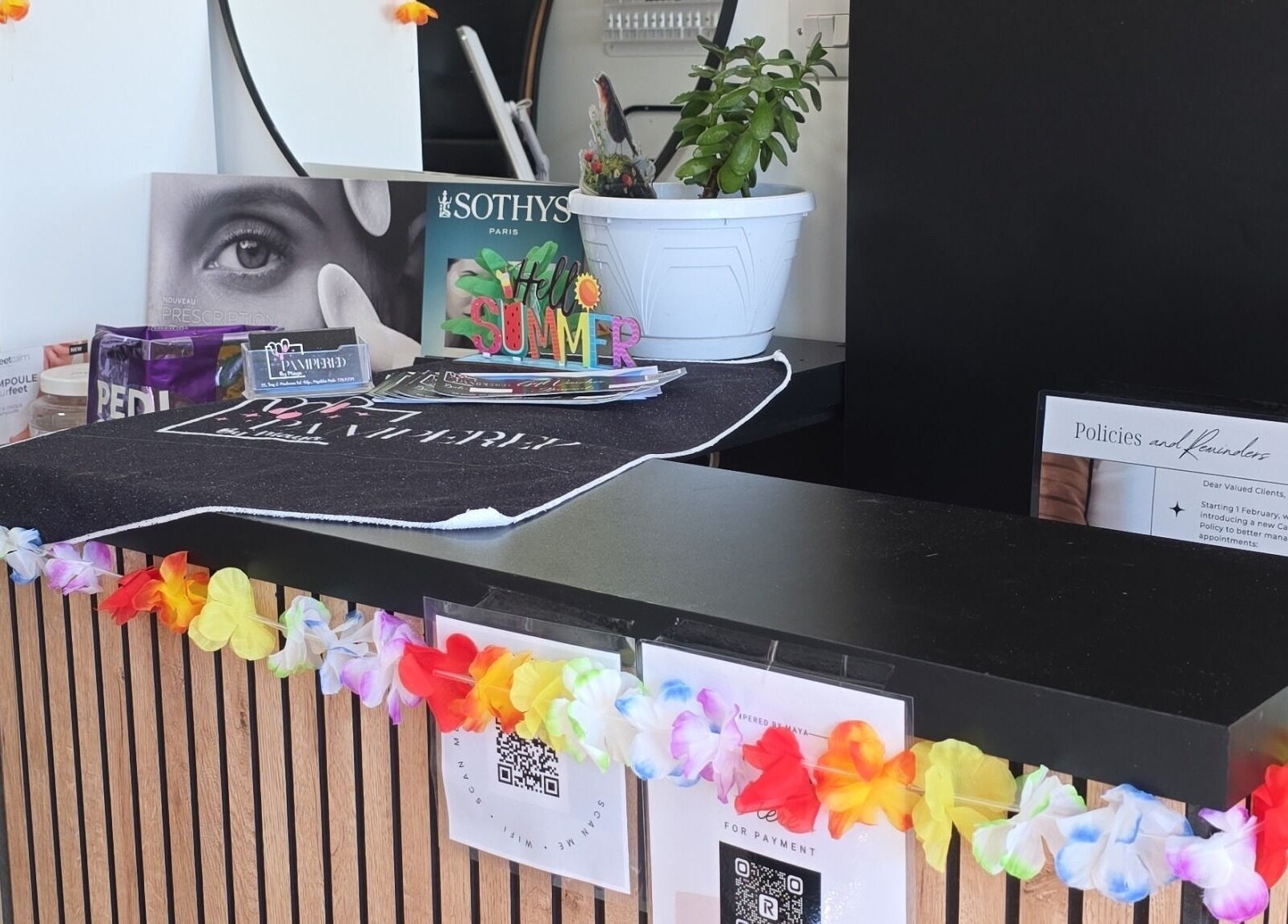 Reception desk at Pampered by Maya, L-imqabba, MT, decorated with colorful garlands and beauty products.