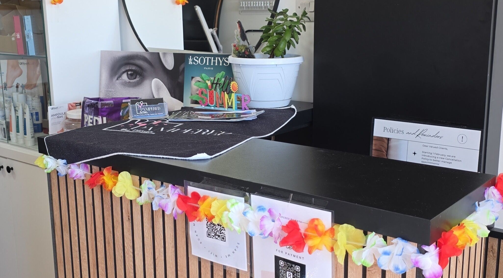 Reception desk at Pampered by Maya, L-imqabba, MT, decorated with colorful garlands and beauty products.