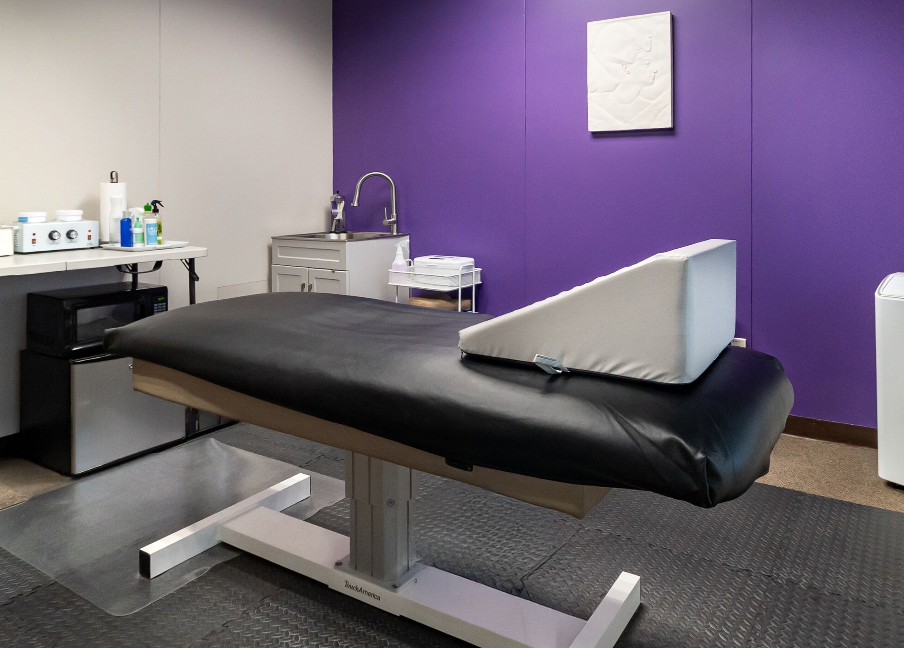 Relaxing treatment room at Sugar Body Eco-Spa, Buffalo, NY featuring a massage table and purple accent wall.
