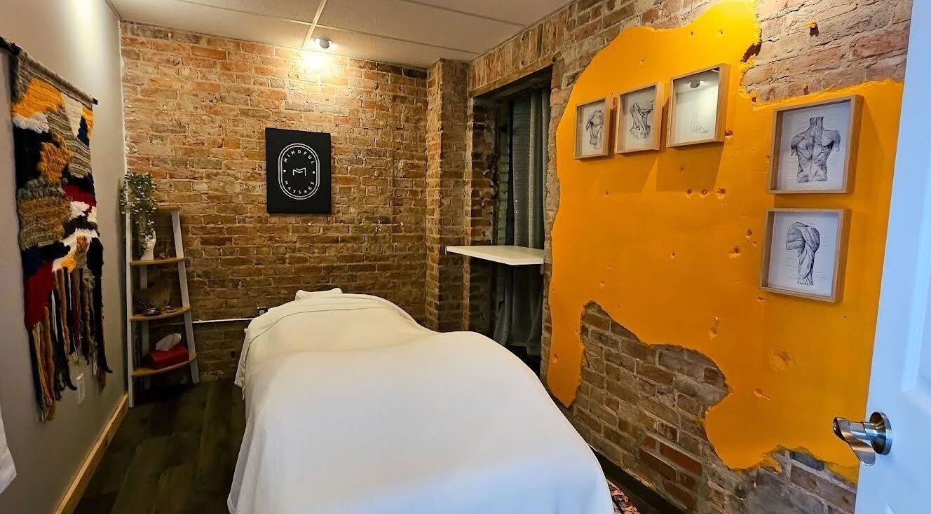 Cozy massage room in Mindful Massage, Pembroke, Ontario with exposed brick and vibrant art.