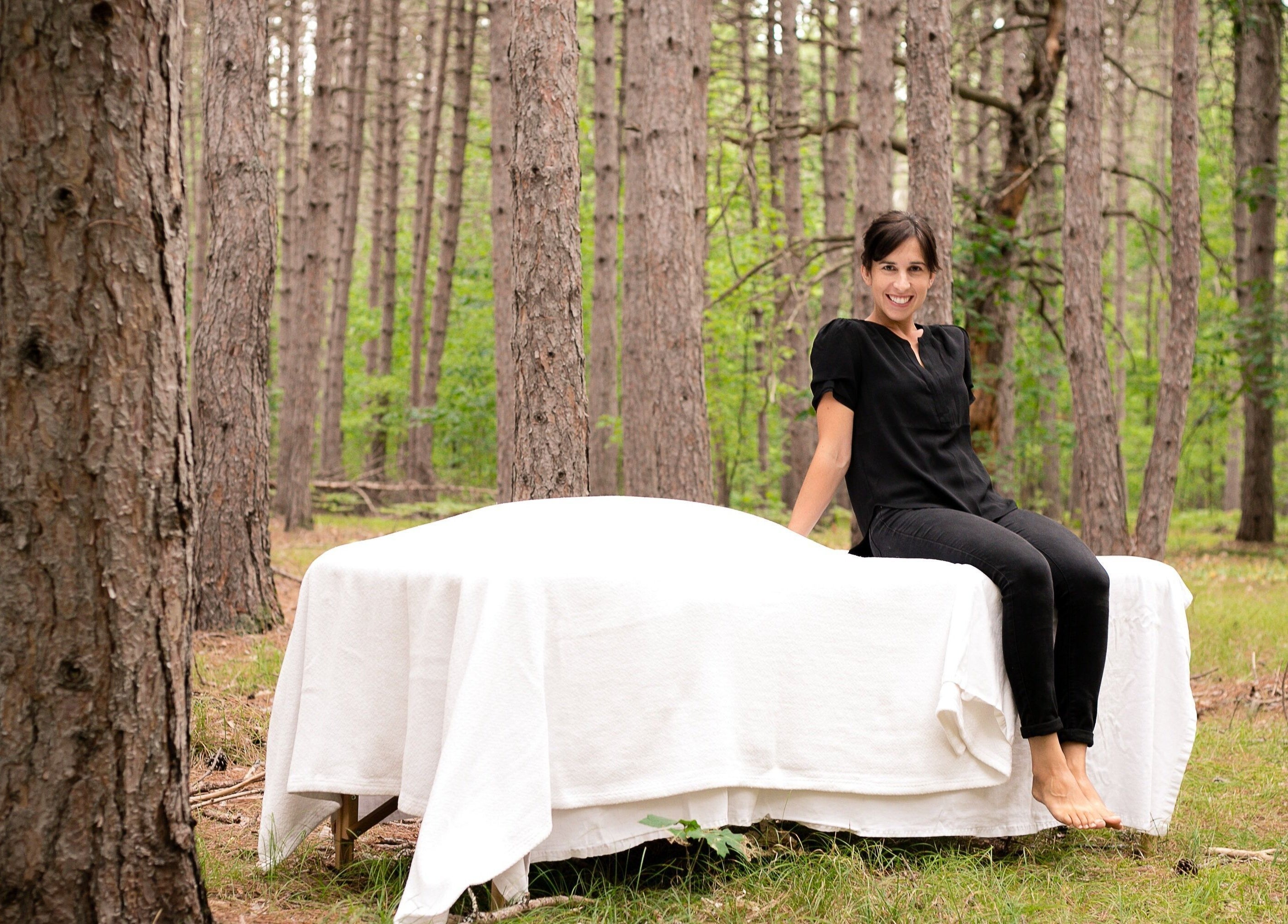 Therapist at Mindful Massage in Pembroke, Ontario, CA, sitting on a table in a tranquil forest setting.