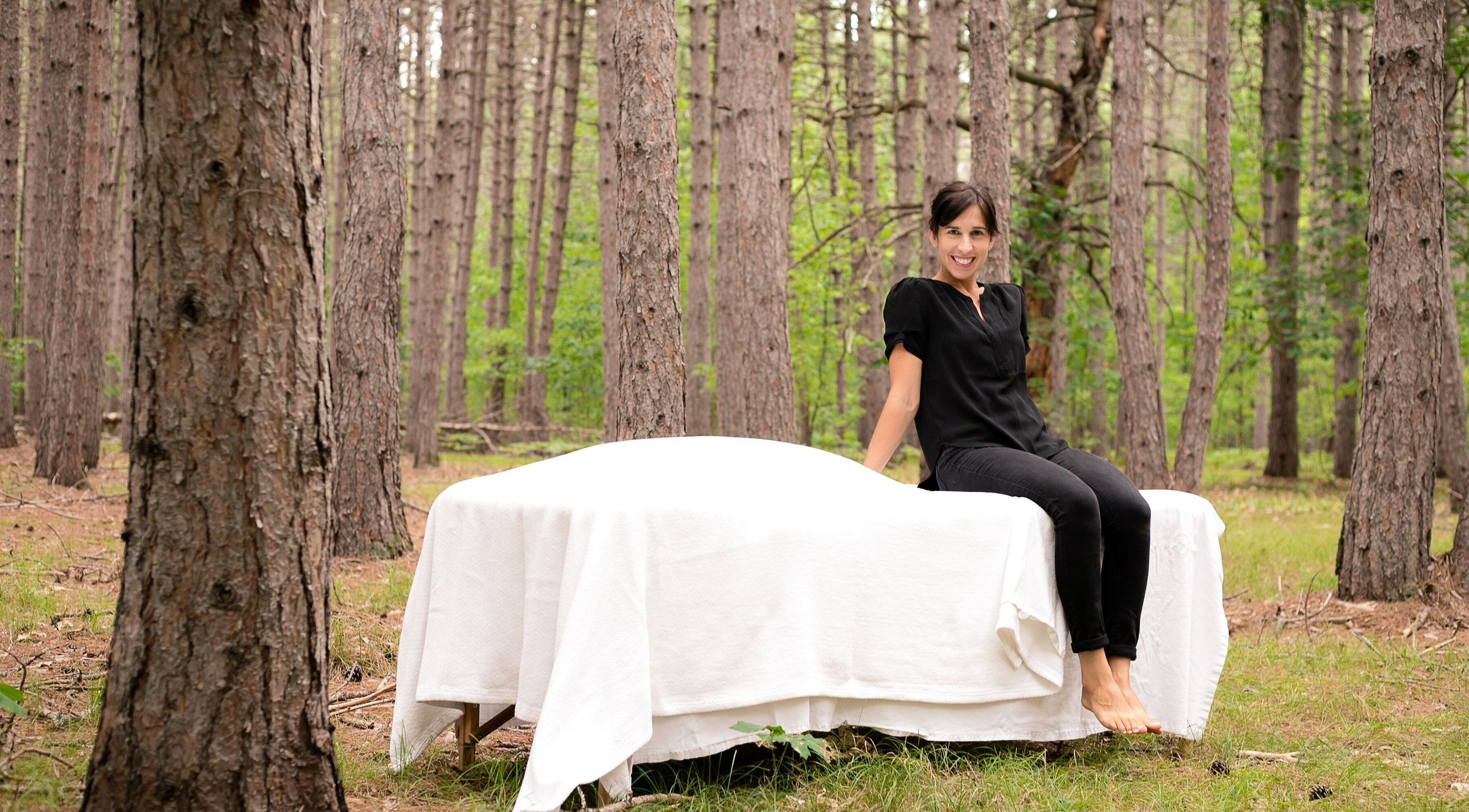 Therapist at Mindful Massage in Pembroke, Ontario, CA, sitting on a table in a tranquil forest setting.