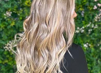Elegant blonde waves hairstyle at Styles By Margarita, Green Bay, Wisconsin, US, with lush greenery backdrop.