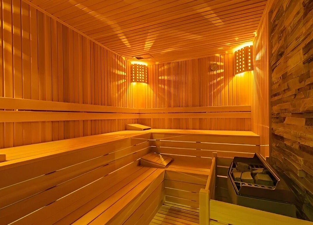 Cozy wooden sauna at Artemis Spa in Poseidon Hotel, Muğla, Muğla, TR, showcasing warm lighting and stone wall.