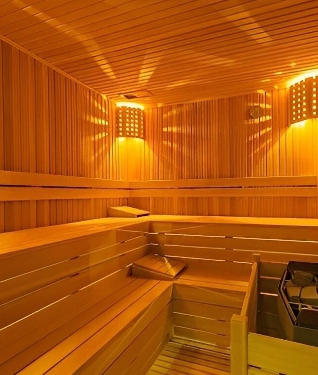 Cozy wooden sauna at Artemis Spa in Poseidon Hotel, Muğla, Muğla, TR, showcasing warm lighting and stone wall.