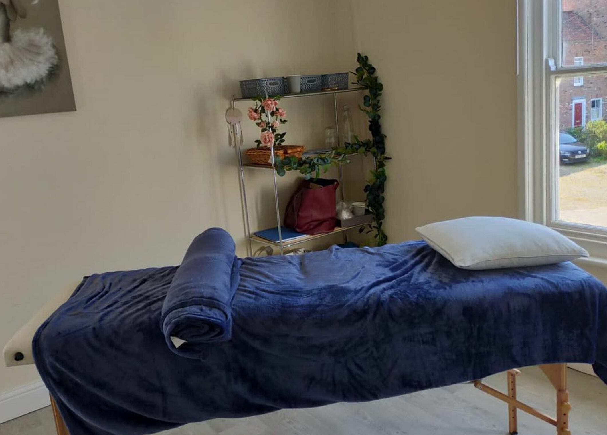 Relaxing massage room at GH Hair Design, King's Lynn, England, GB with a cozy treatment table by a window.