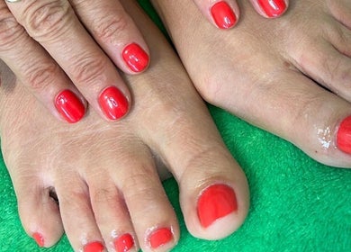 Fresh red manicure and pedicure at 19 Beauty Room, Leigh, England, GB on green towel.
