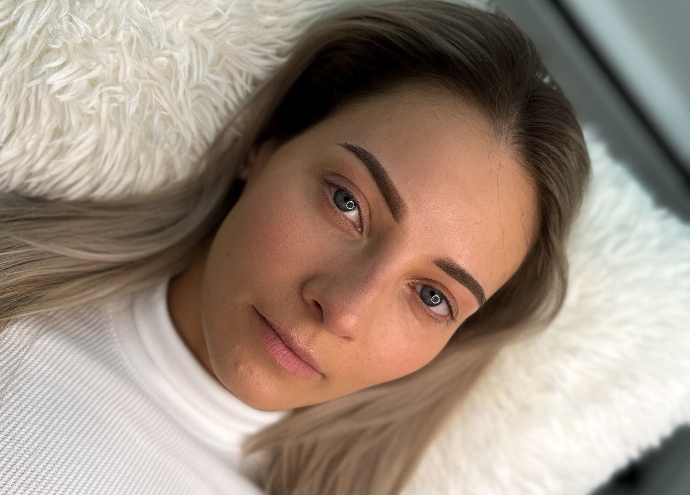 Client with beautifully shaped eyebrows, styled at The Brow Mami in Hamilton, Ontario, CA, relaxing on a plush pillow.