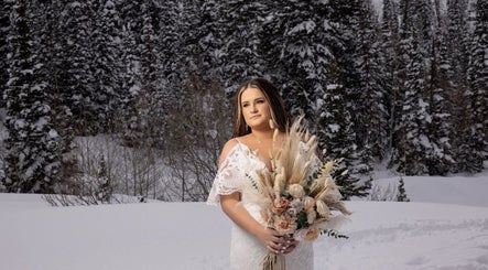 Bride in snow, holding bouquet at Meg You Glow in Heber City, Utah, US, surrounded by snow-covered trees.
