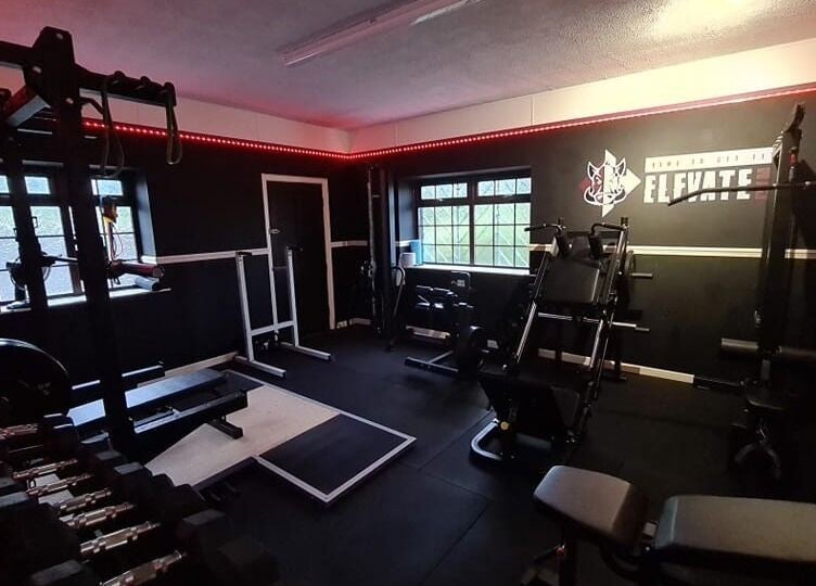 Modern gym interior at Elevate Gym + Athlete Recovery in Clogher, Northern Ireland, GB with equipment and red lighting.