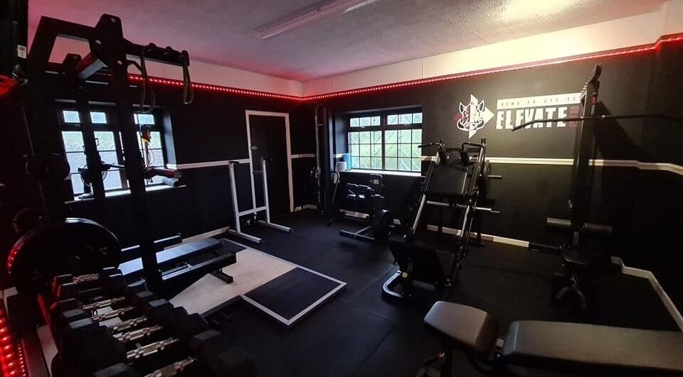 Modern gym interior at Elevate Gym + Athlete Recovery in Clogher, Northern Ireland, GB with equipment and red lighting.