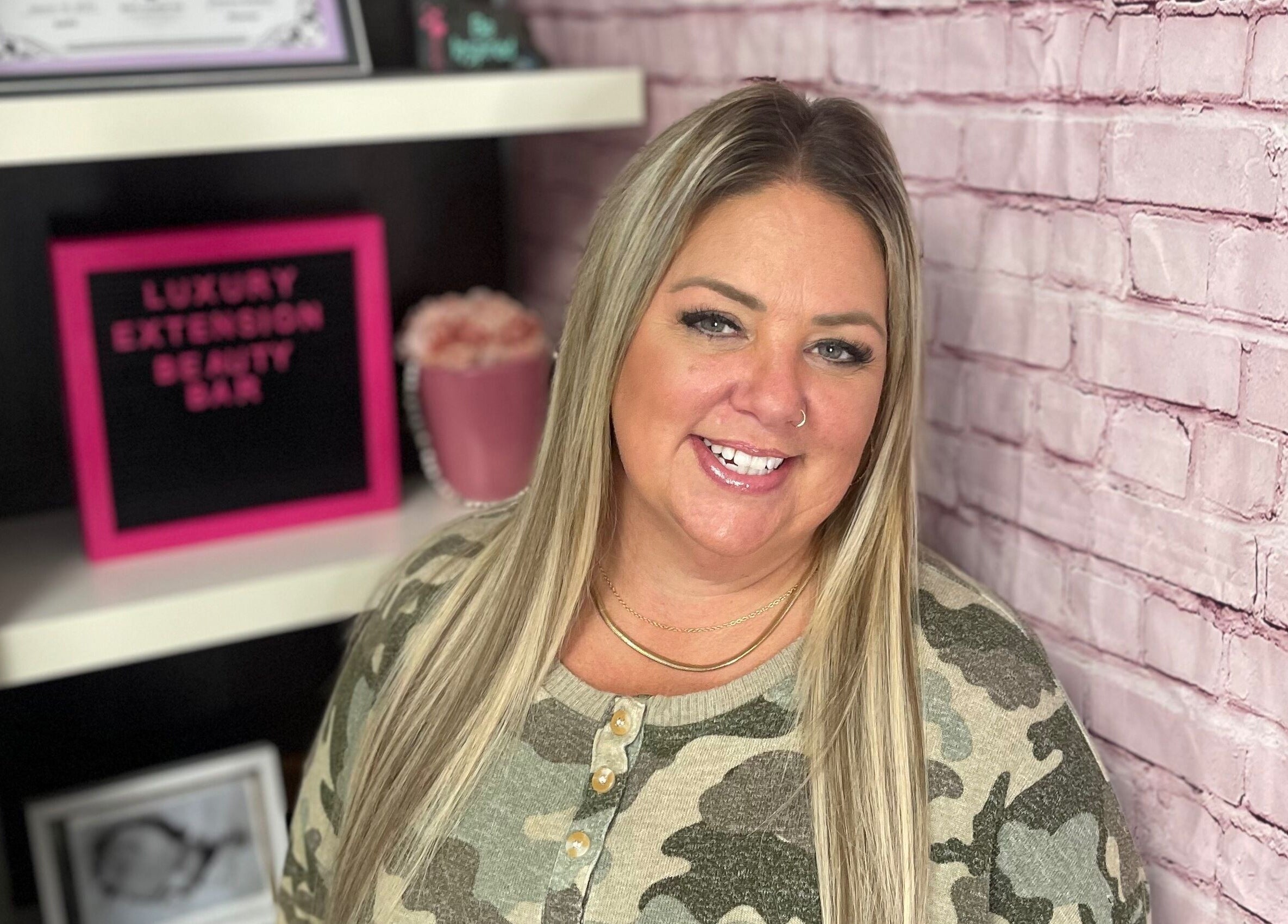 Professional at Orillia & Area Luxury Extension Beauty Bar, Orillia, Ontario, CA, smiling by pink brick wall.