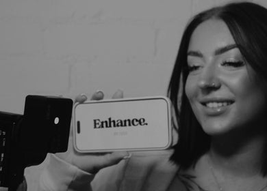 Smiling woman holding a phone displaying 'Enhance by Han' logo at Christchurch, GB.