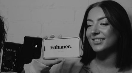 Smiling woman holding a phone displaying 'Enhance by Han' logo at Christchurch, GB.