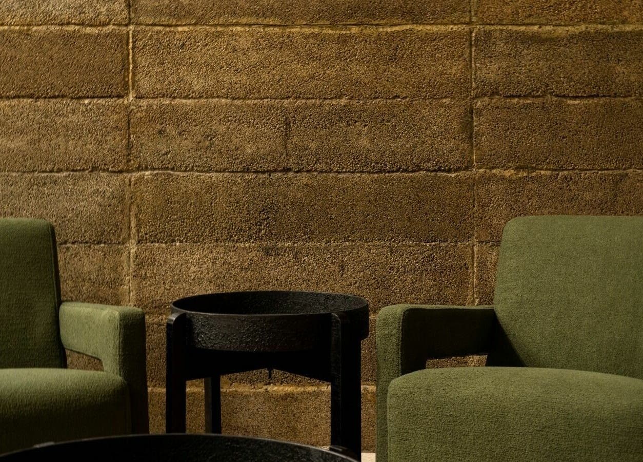 Relaxation seating area at Float Barbershop, Sharjah, AE with green chairs and a rustic wall backdrop.