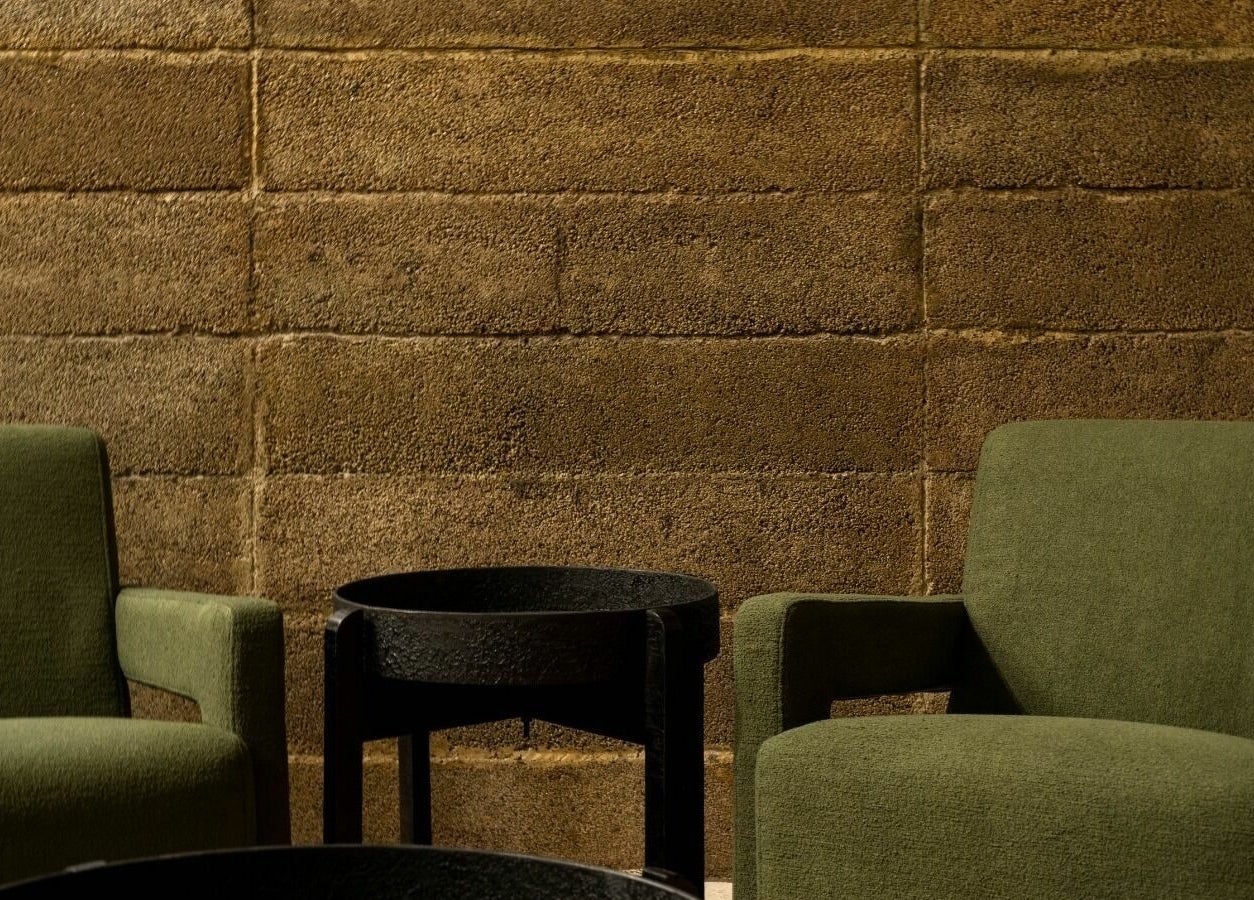 Relaxation seating area at Float Barbershop, Sharjah, AE with green chairs and a rustic wall backdrop.