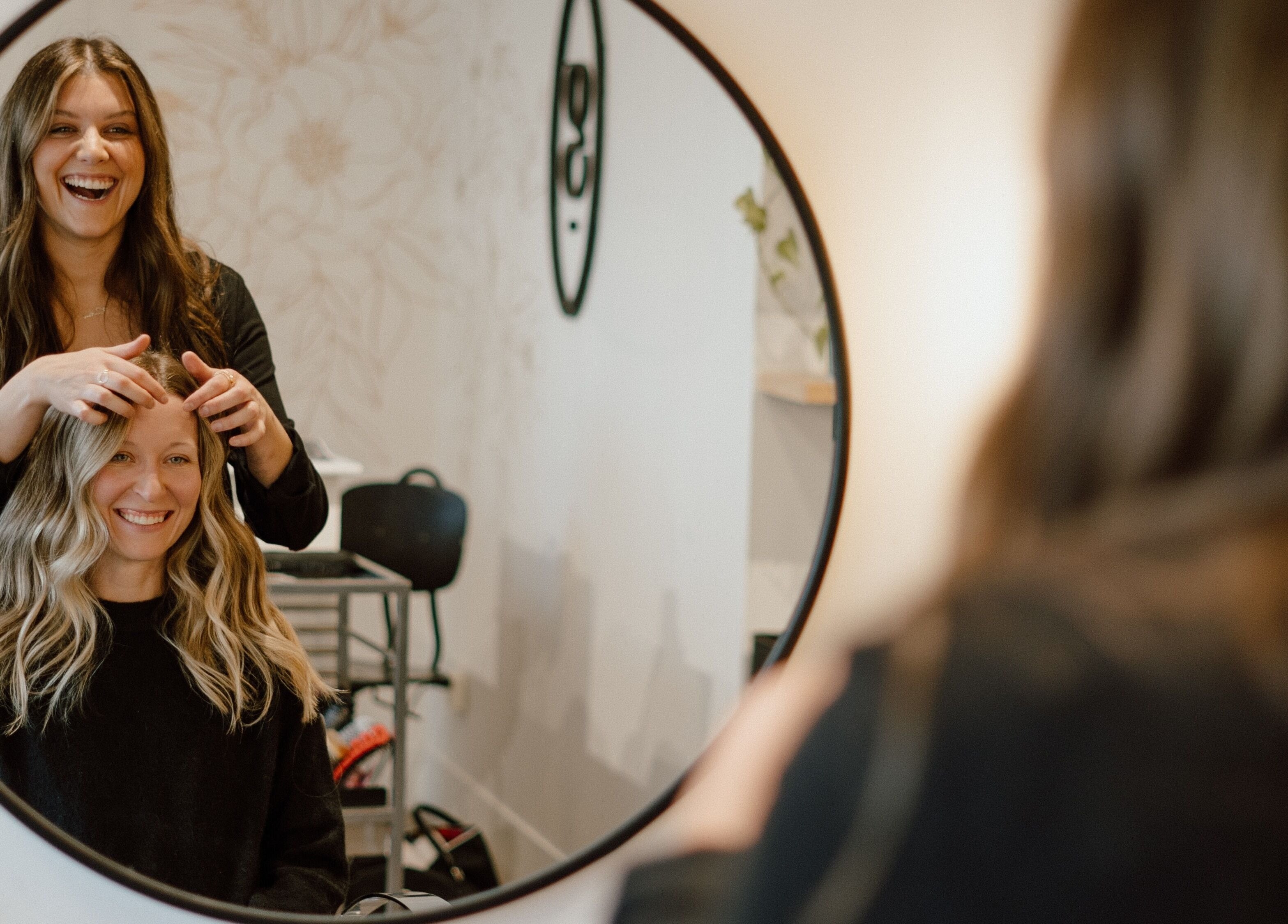 Stylist working on customer's hair at Glow Hair Studio, Thorold, Ontario, CA, both smiling in mirror.