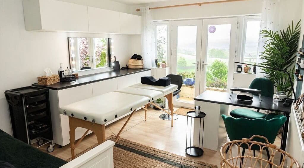Relaxing treatment room at Flos’ Beauty Box, Stroud, England, GB with massage table and lush greenery.