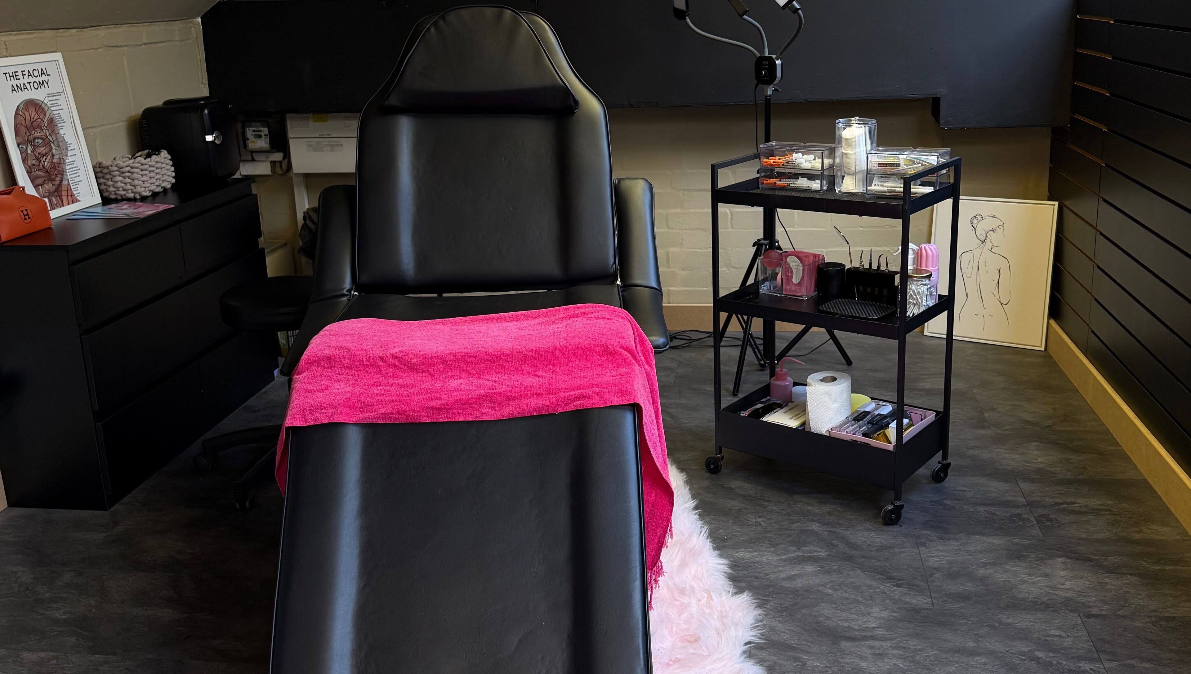 Treatment room at Aesthetic Atelier in Crawley, England, GB with a luxurious black chair and vibrant pink towel.