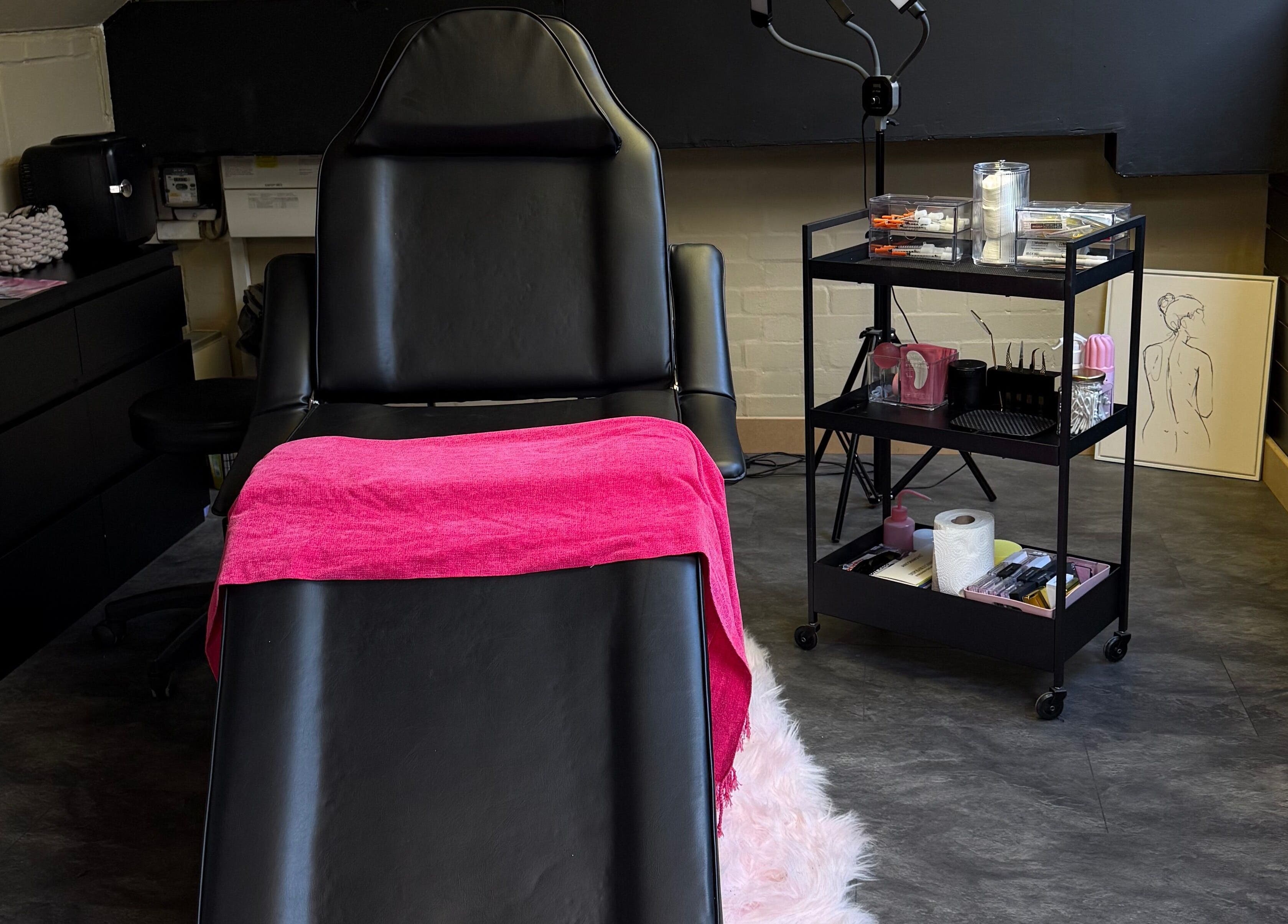 Treatment room at Aesthetic Atelier in Crawley, England, GB with a luxurious black chair and vibrant pink towel.