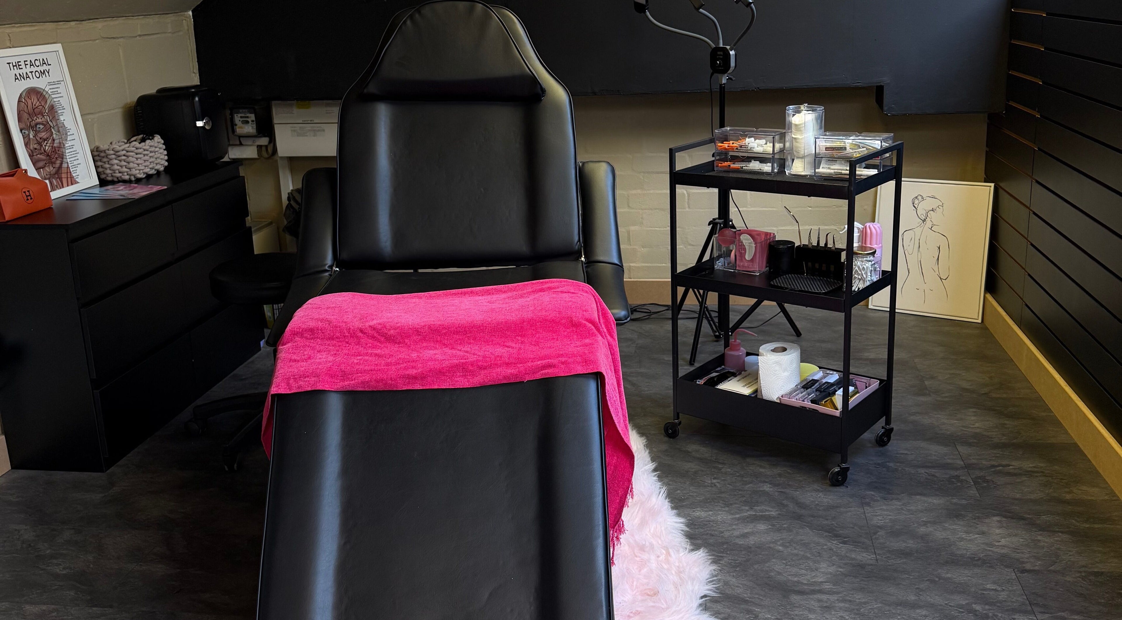 Treatment room at Aesthetic Atelier in Crawley, England, GB with a luxurious black chair and vibrant pink towel.
