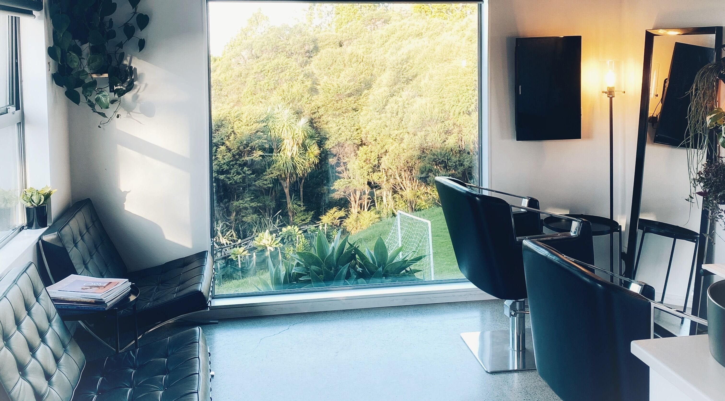Bright salon interior at Equinox Hair, Auckland, NZ with stylish chairs and a scenic garden view.