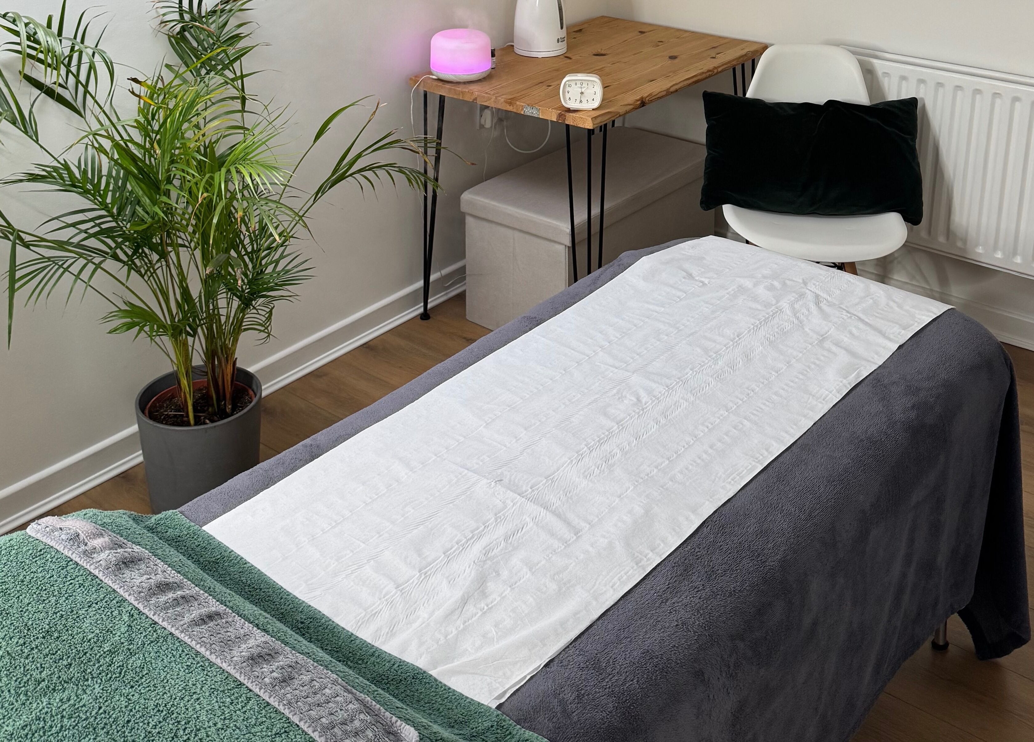 Serene massage room at Natural Beauty Cardiff, Cardiff, Wales, GB with a cozy treatment bed and potted plants.