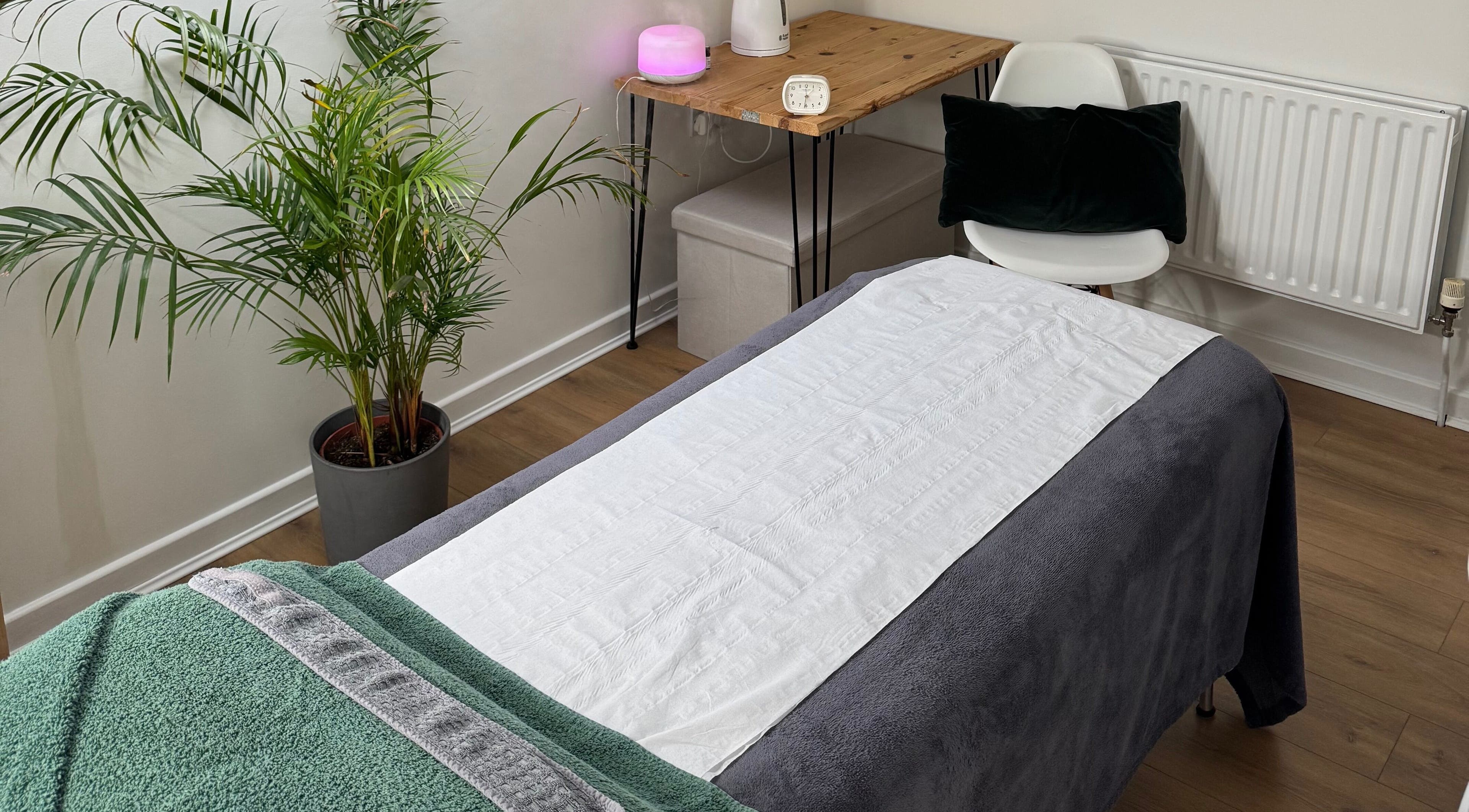 Serene massage room at Natural Beauty Cardiff, Cardiff, Wales, GB with a cozy treatment bed and potted plants.