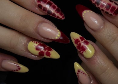 Intricate nail art designs at Nail Luxe, Nantwich, England, GB. Red and yellow patterns on almond-shaped nails.