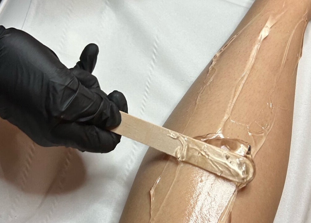 Leg waxing service at Elevate, Ripon, England, GB. Black-gloved hand applying wax with a spatula.