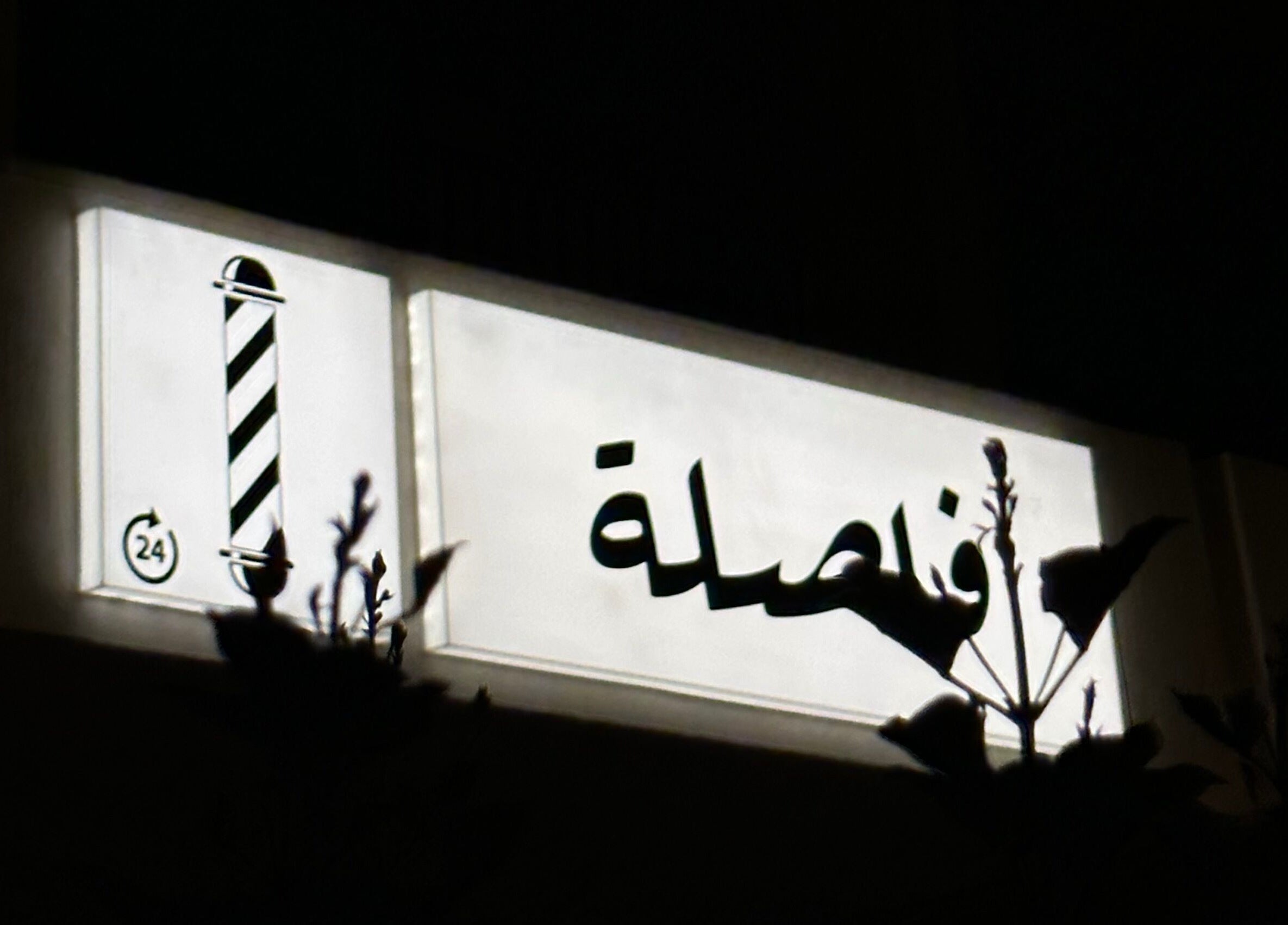 Illuminated sign of Comma Barber in Riyadh, Riyadh Province, SA, displaying traditional barber pole.