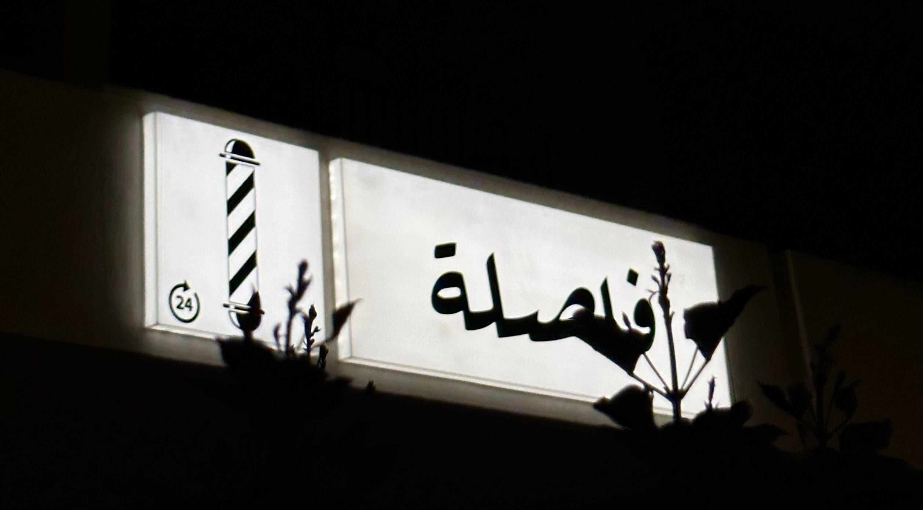 Illuminated sign of Comma Barber in Riyadh, Riyadh Province, SA, displaying traditional barber pole.