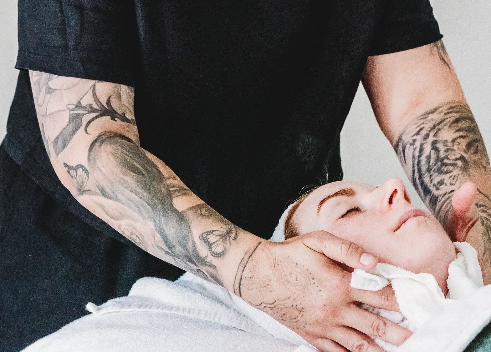 Tattooed therapist giving a facial massage at Exhale Holistic Skin in Bentleigh East, Victoria, AU.