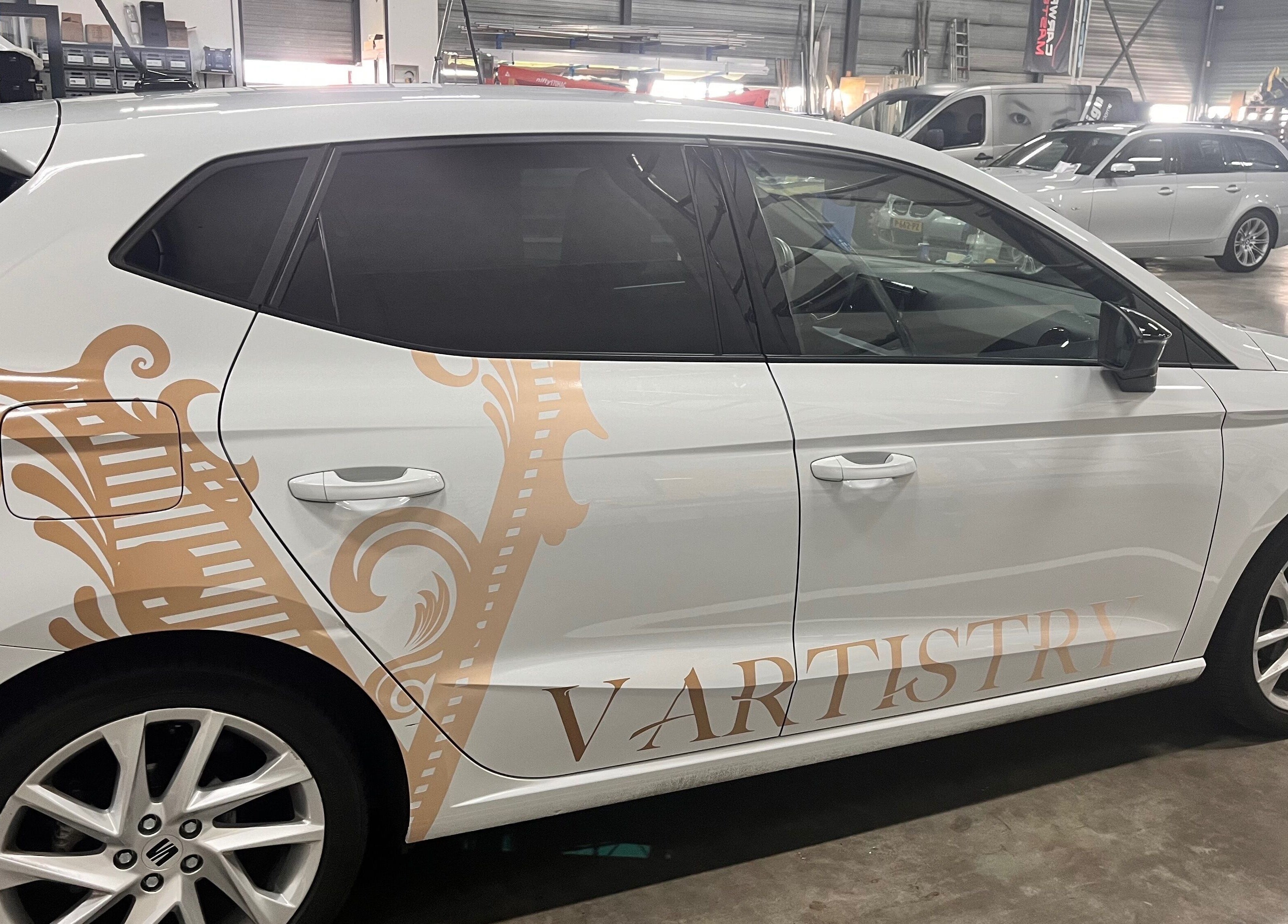 Beschilderde auto met V Artistry logo in werkplaats, Ravels, Vlaanderen, BE.