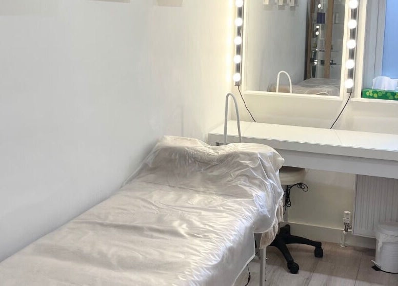 Treatment room at Madison Aesthetics, Berkhamsted, England, GB, featuring a bed and vanity with lit mirror.