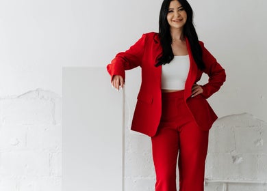 Professional stylist at Hairby_maha in Windsor, Ontario, CA, wearing a chic red suit and smiling confidently.
