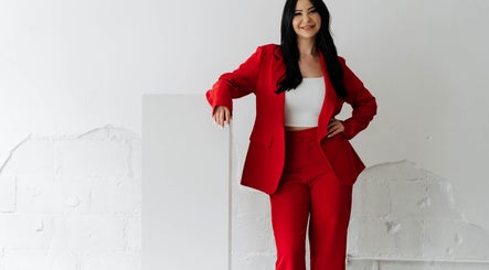 Professional stylist at Hairby_maha in Windsor, Ontario, CA, wearing a chic red suit and smiling confidently.