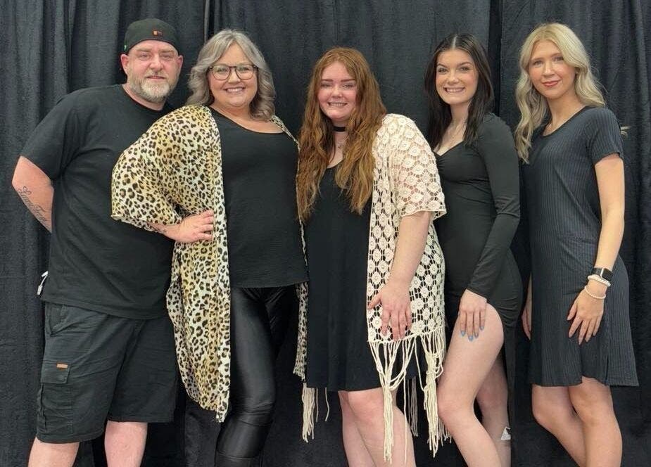 Legacy Salon team in Warrensburg, Missouri, US, smiling in stylish attire against black curtains.