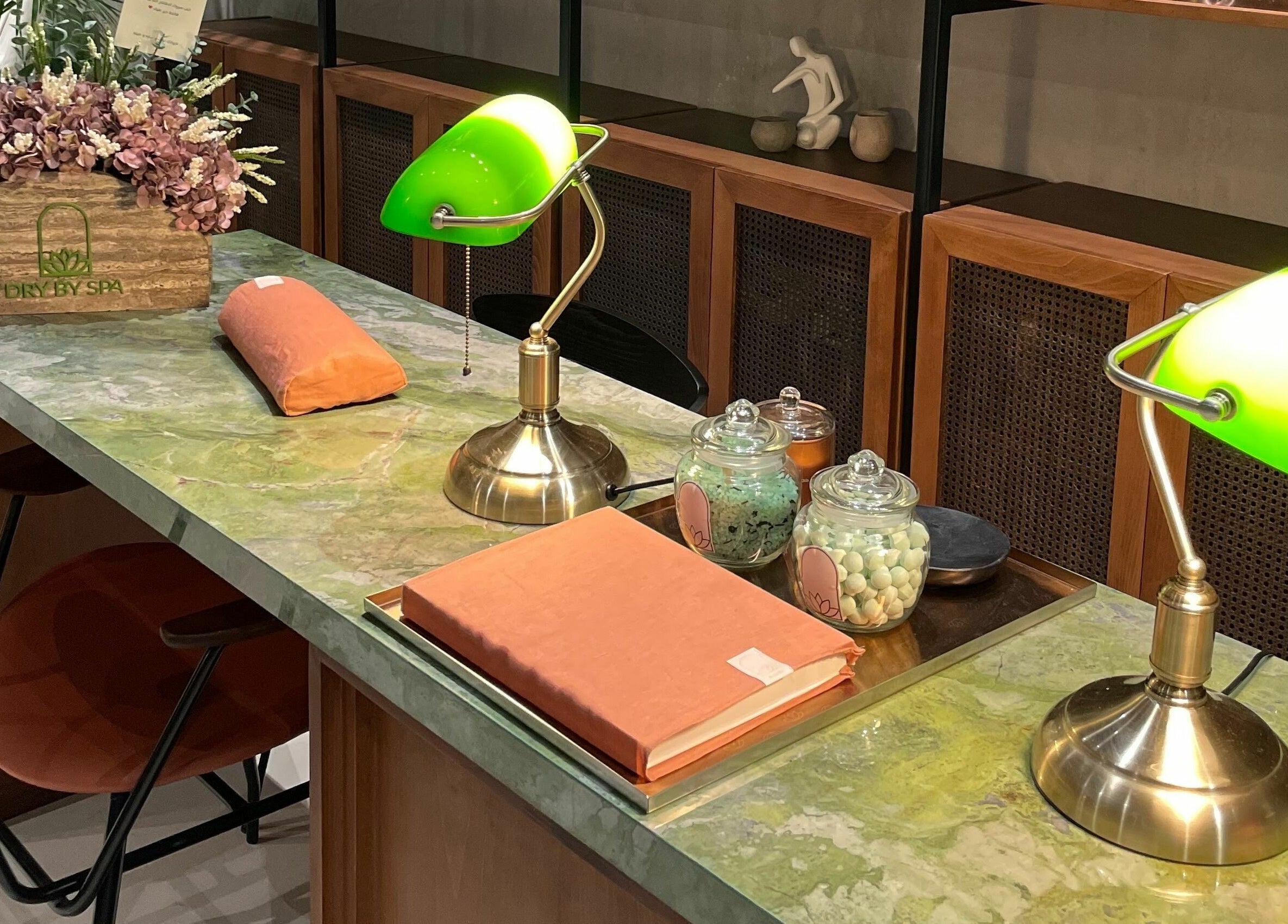 Chic spa reception at Dry by Spa, Riyadh, SA with vintage lamps and floral decor on a marble counter.