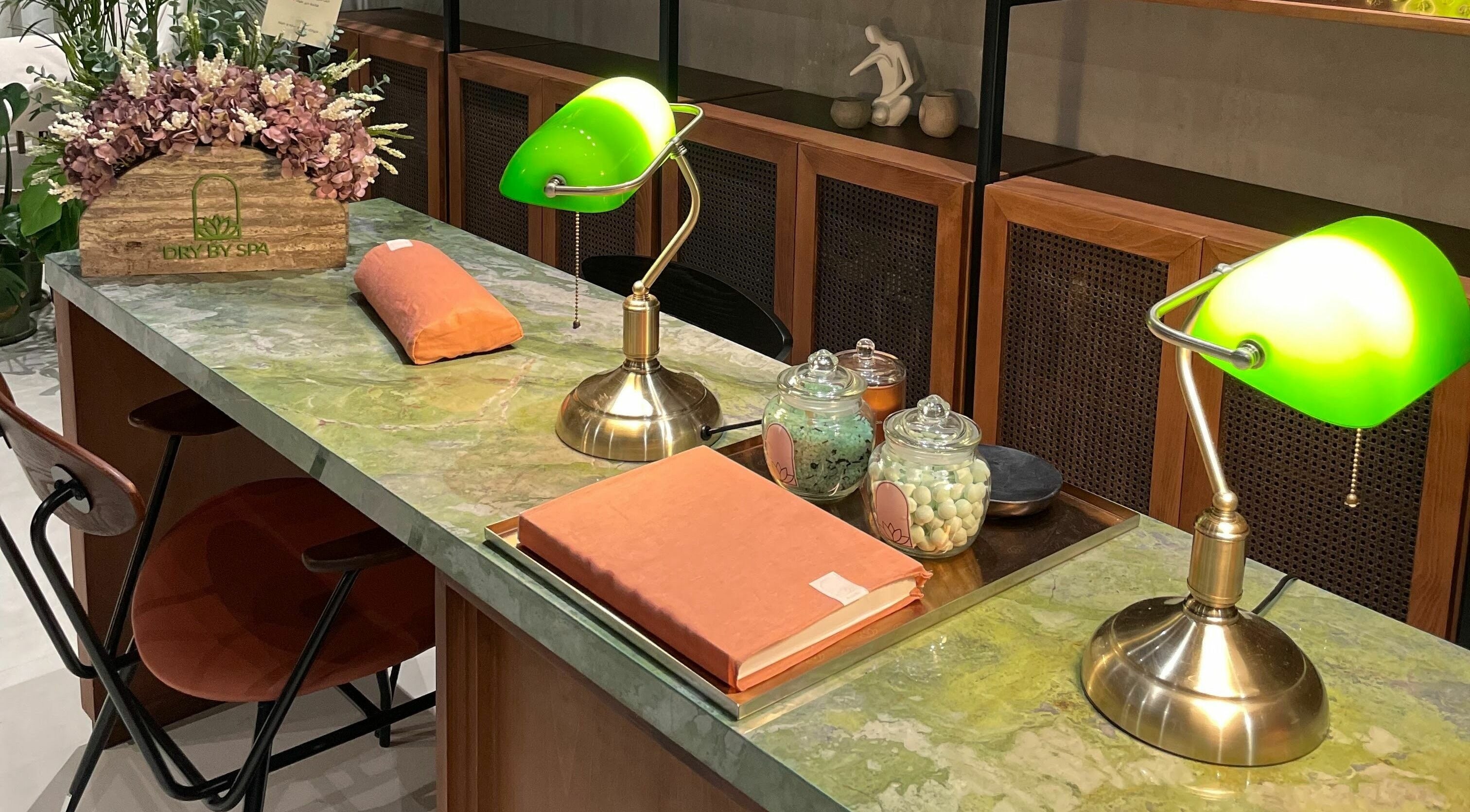 Chic spa reception at Dry by Spa, Riyadh, SA with vintage lamps and floral decor on a marble counter.